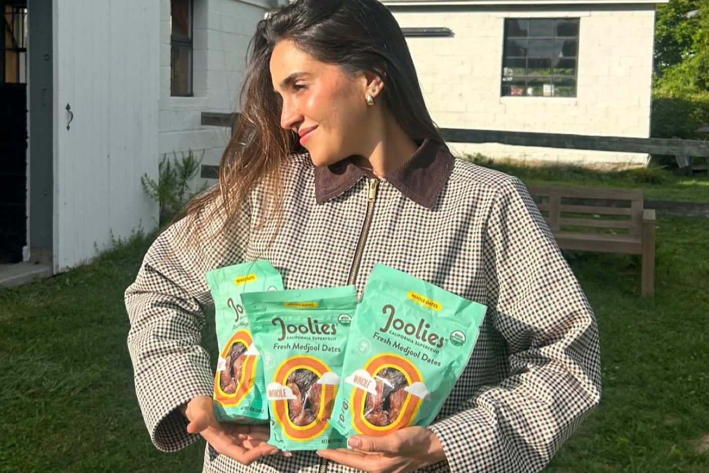 woman holding three packages of joolies dates standing outside in the sun smiling